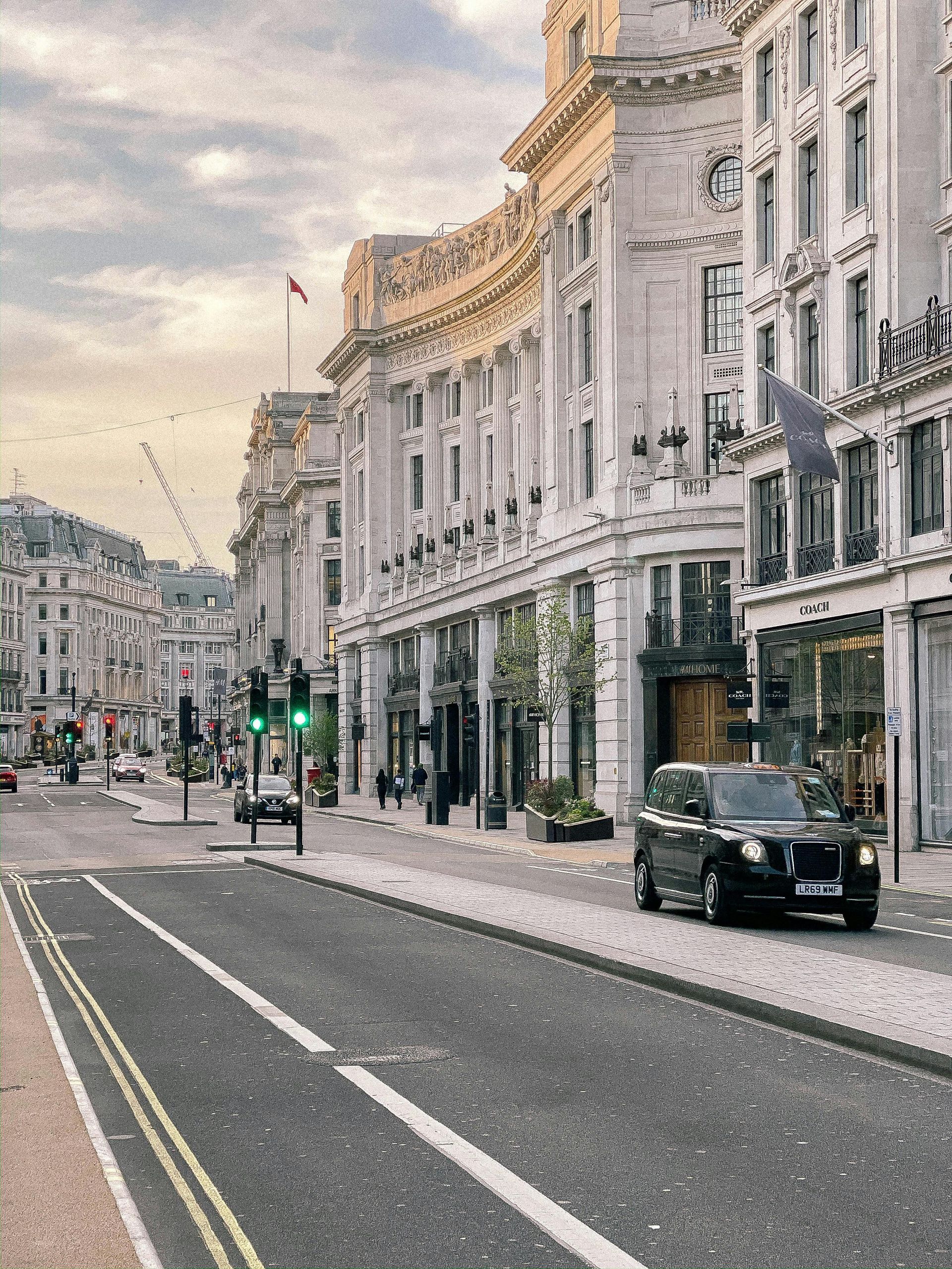 Street view of London with classic architecture, a black cab, and a cloudy sky.