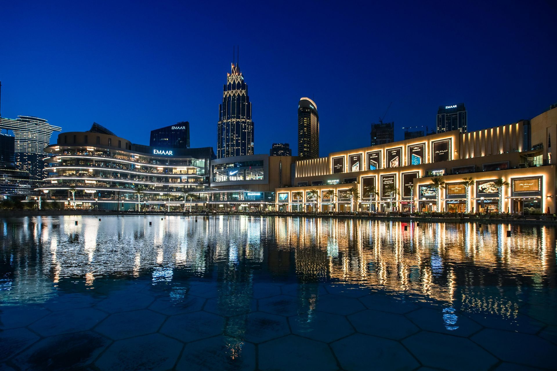 Buildings illuminated at night reflected in water, Dubai. Blue sky, bright lights.