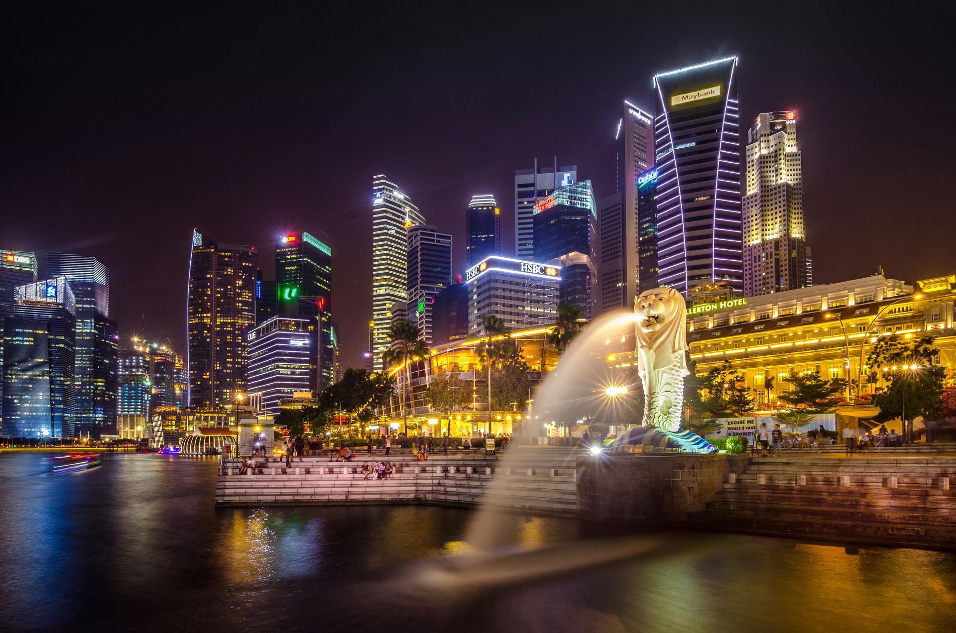 The Merlion statue fountain illuminated at night in front of the modern, glowing skyscrapers of Singapore.