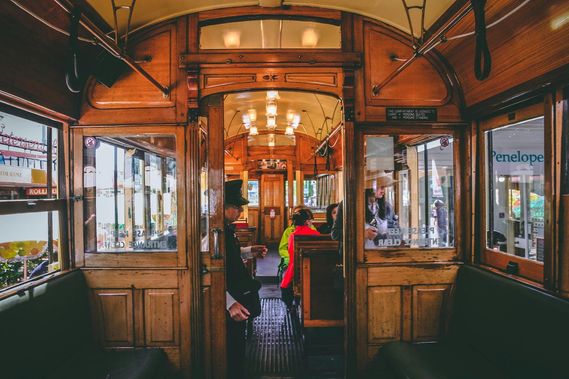 Inside of a classic wooden tram car with passengers and a conductor in a top hat.