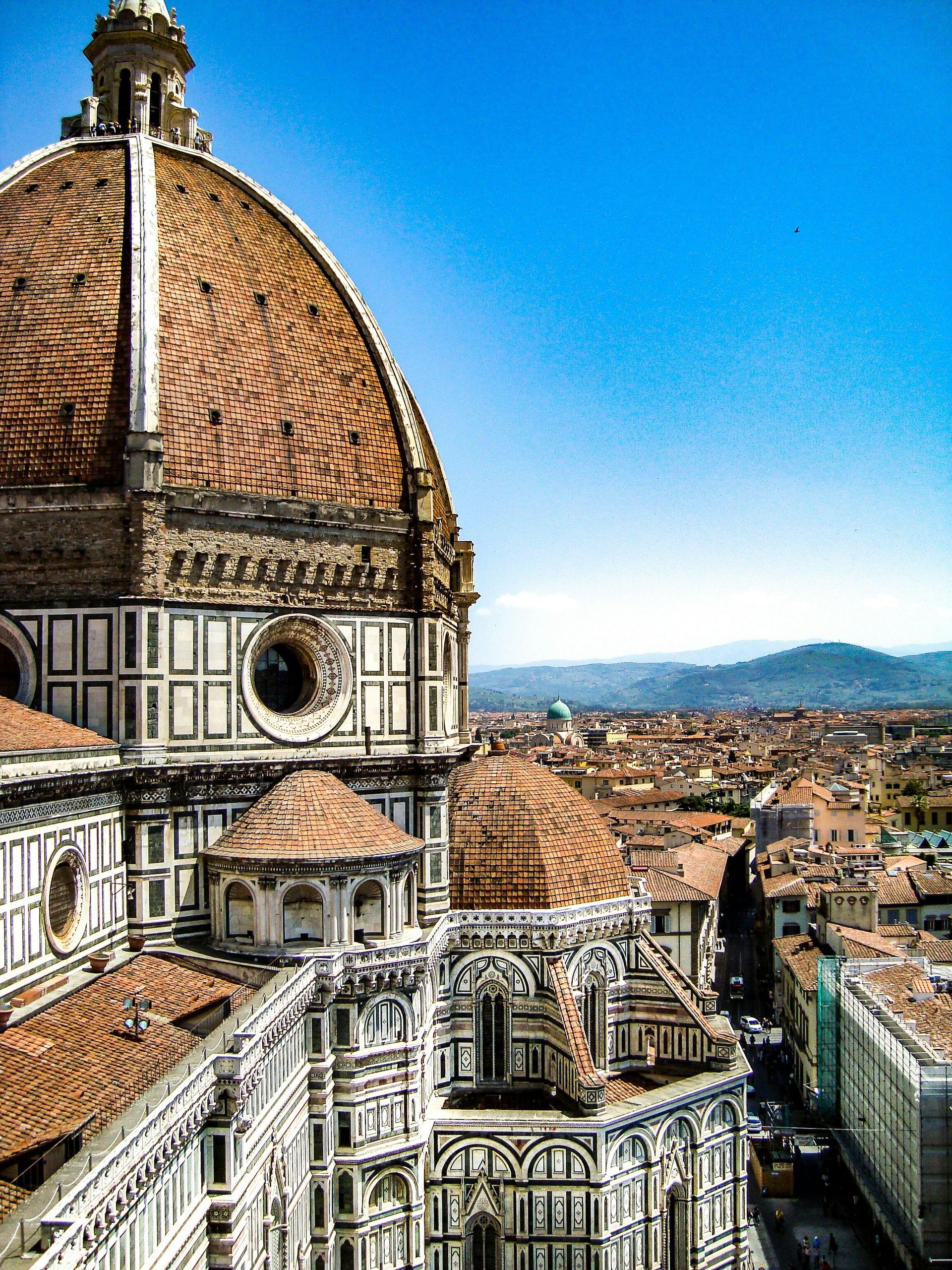 Florence Cathedral's terracotta dome and cityscape against a blue sky.