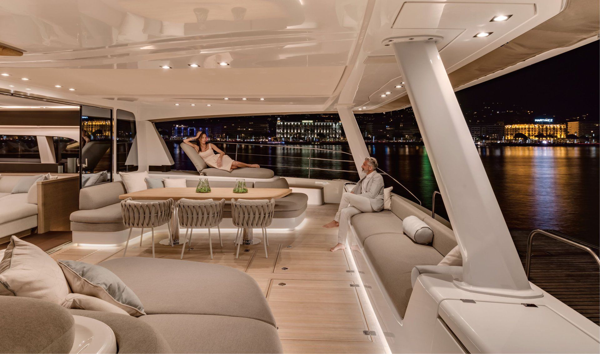 Luxury yacht deck at night with city lights in the background. People lounging and relaxing.