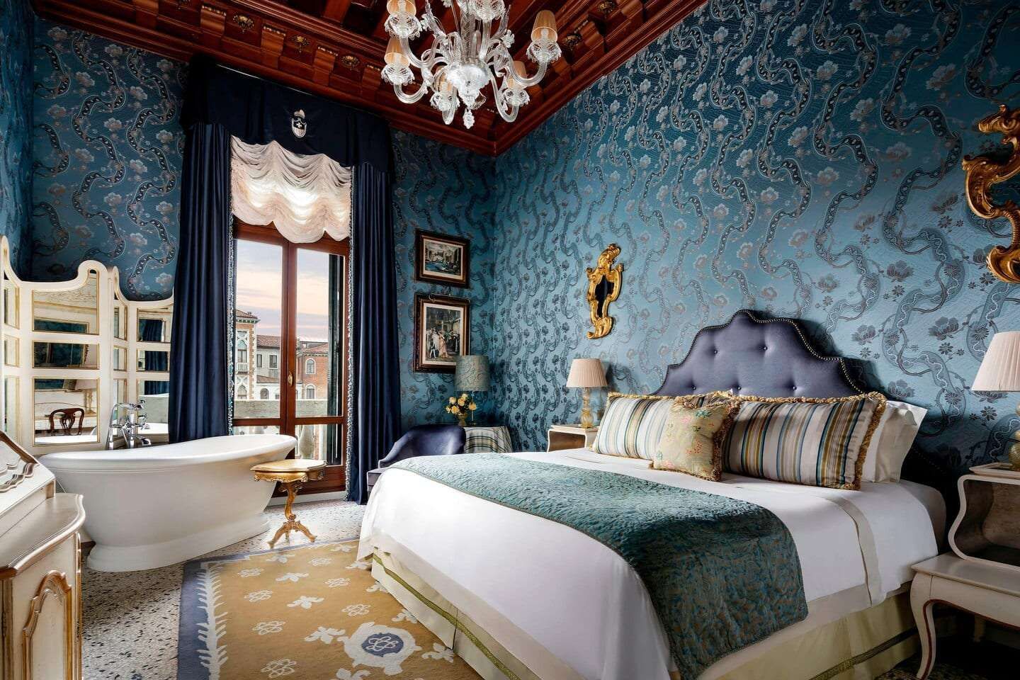 Luxurious bedroom with blue patterned walls, ornate ceiling, large bed, bathtub near a window. The Gritti Palace 