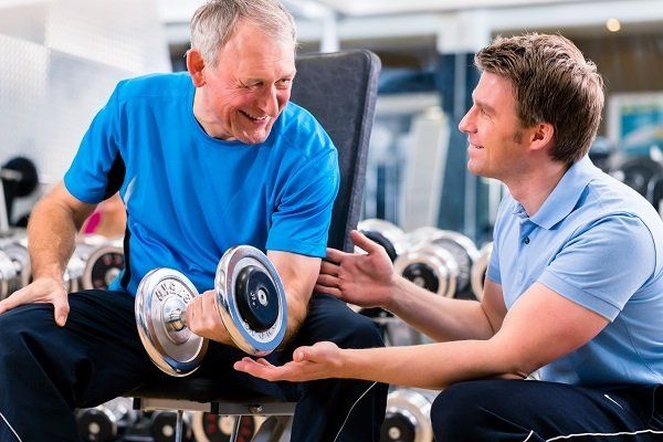 Old man performing weight training whilst being trained by an exercise physiologist