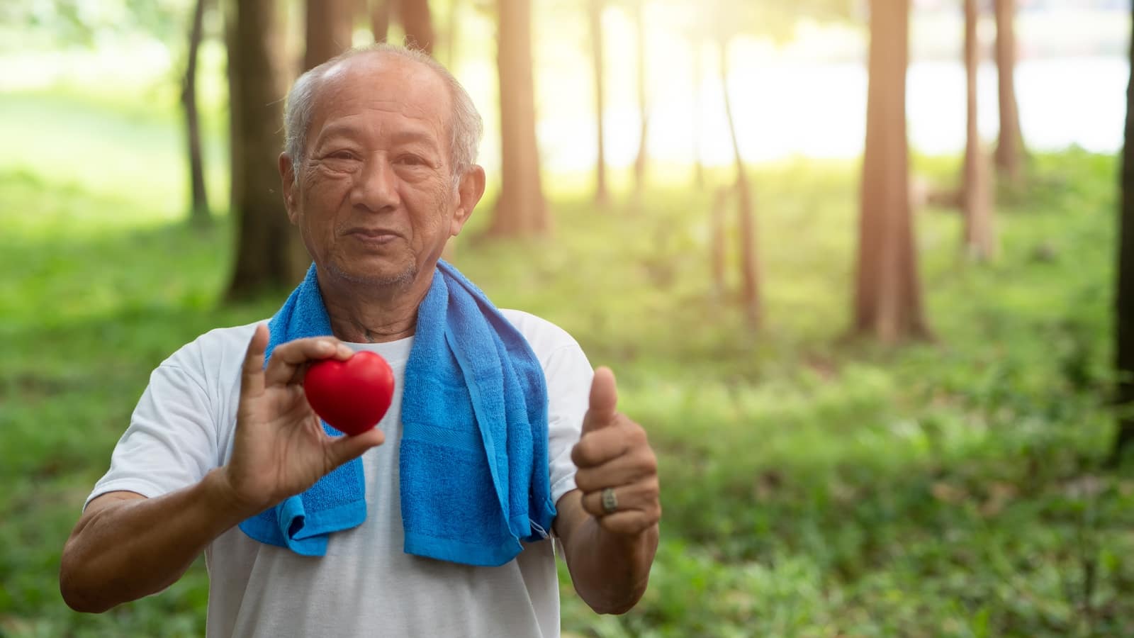 Old man walking in a forest in gym attire whilst eating an apple to improve his heart health