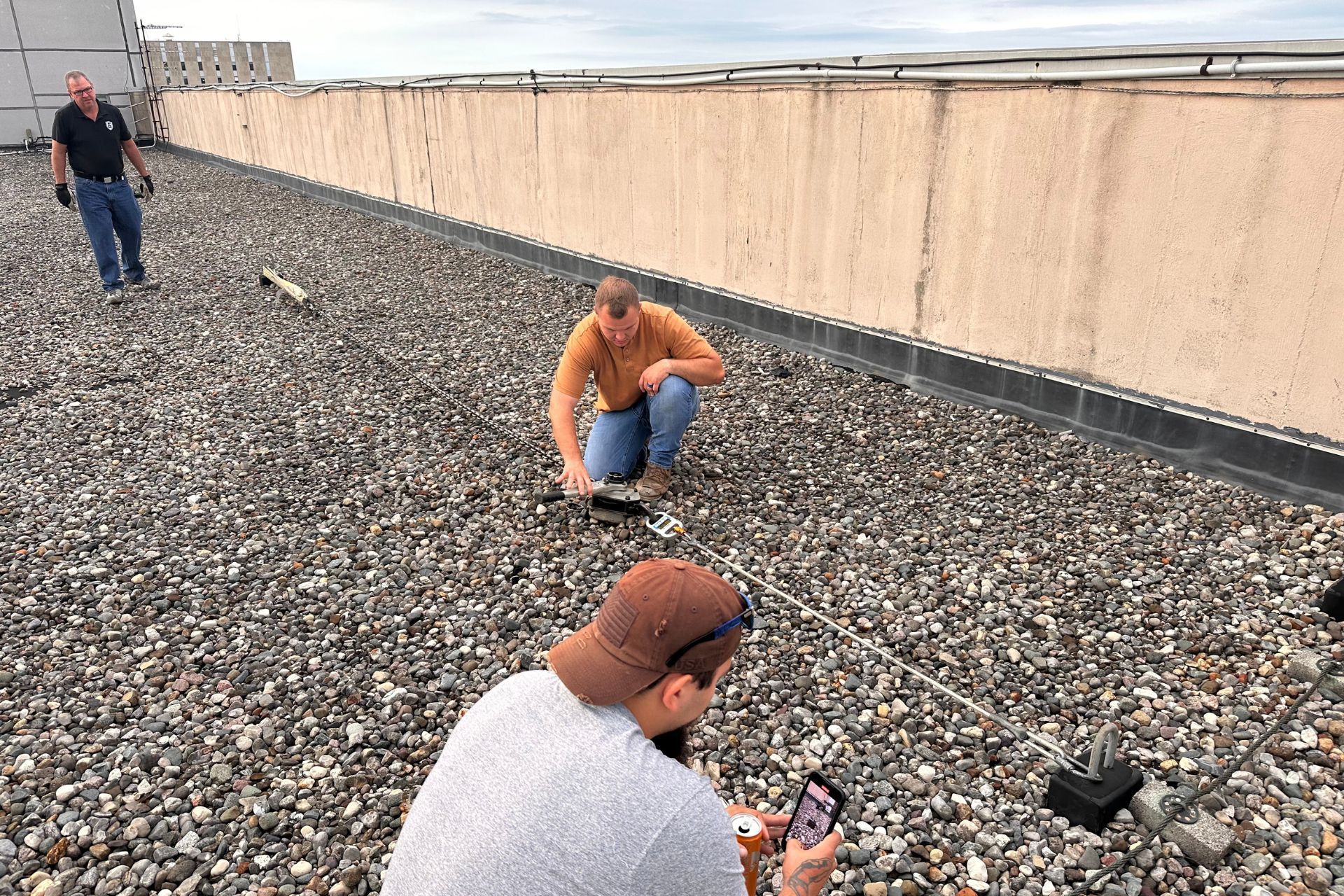 A man is kneeling on a rocky roof while another man looks on.