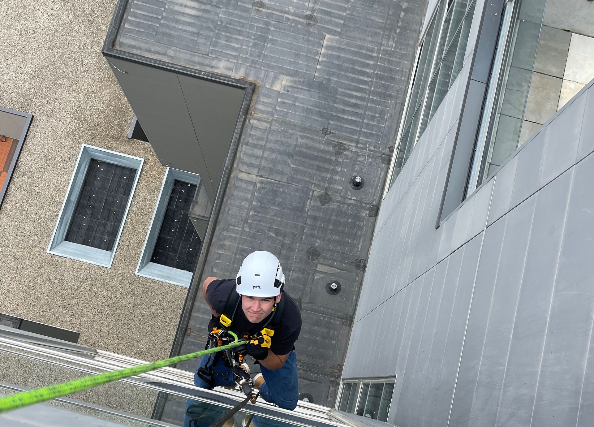 A man wearing a helmet is climbing a rope on the side of a building.