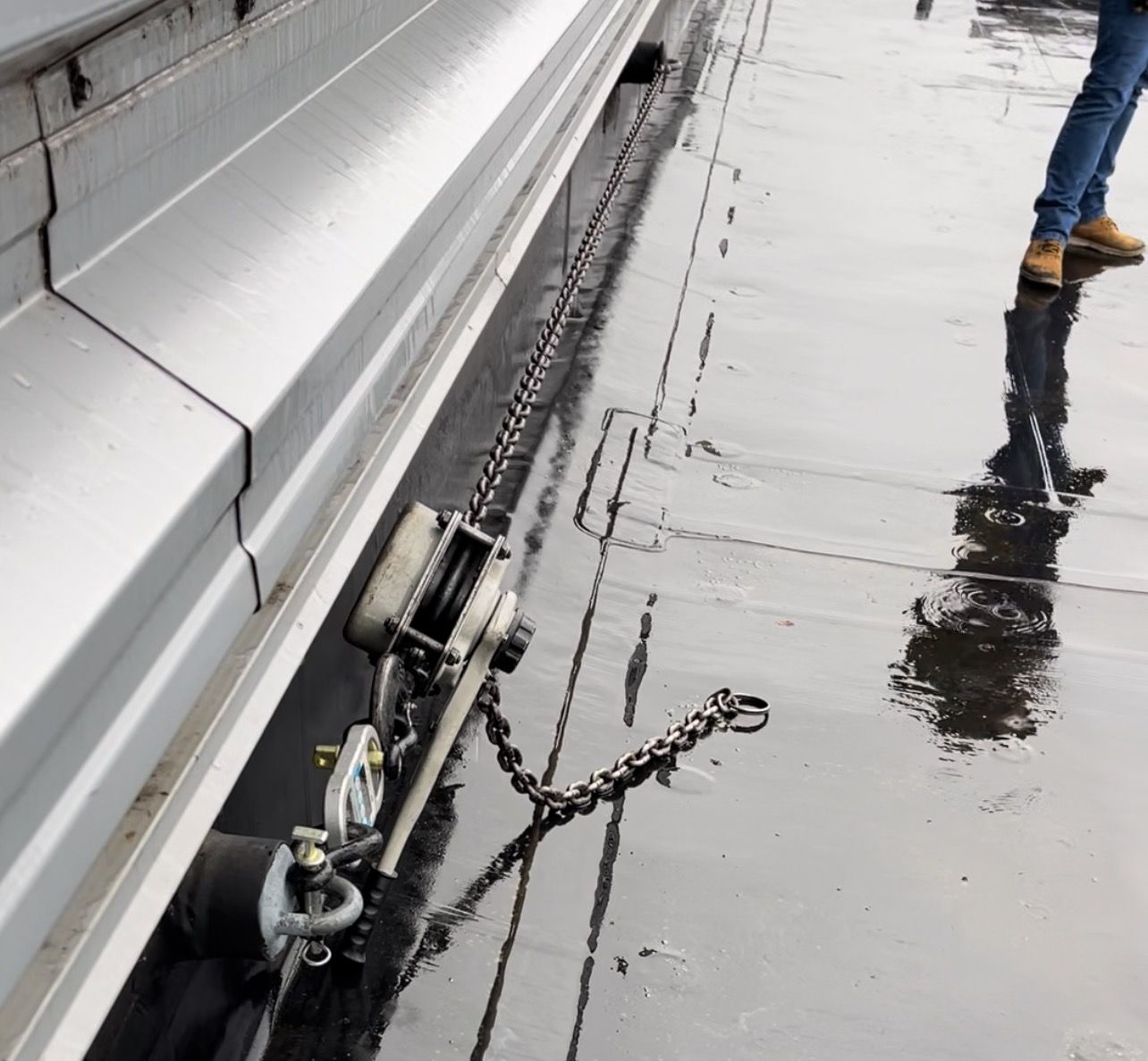 A person is walking on a wet sidewalk next to a chain