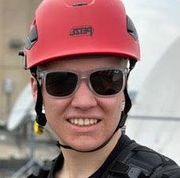 A man wearing a red helmet and sunglasses is smiling.