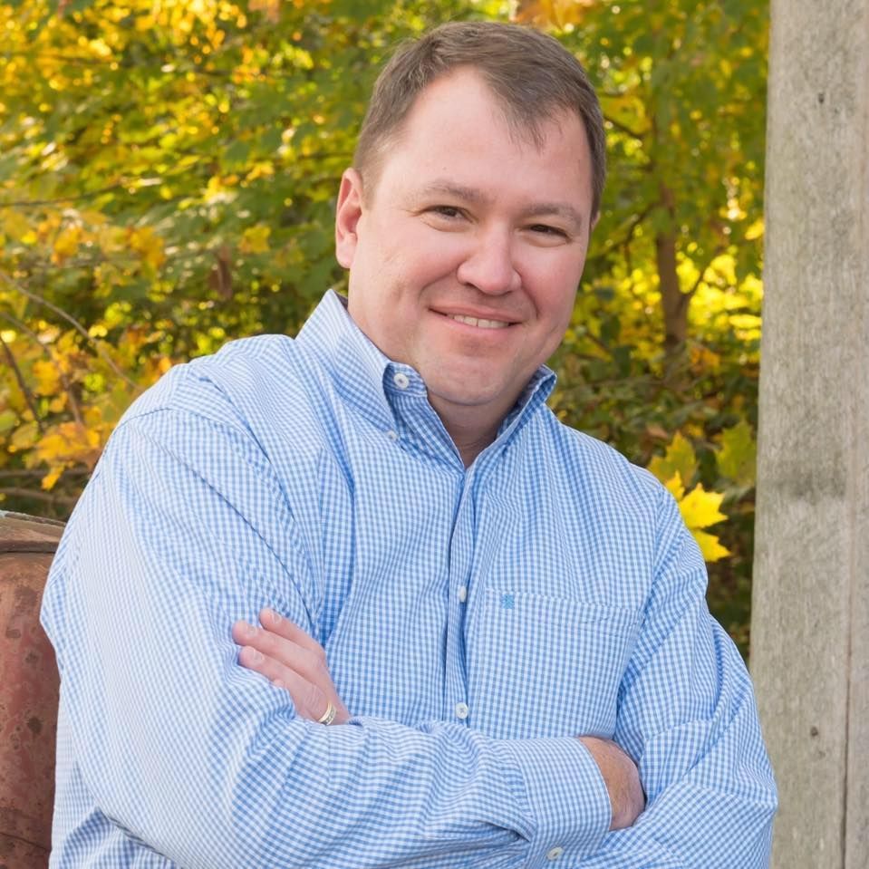 A man in a blue shirt with his arms crossed smiles for the camera