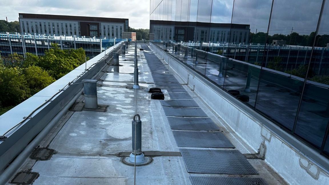 A rooftop walkway leading to a building with trees in the background.