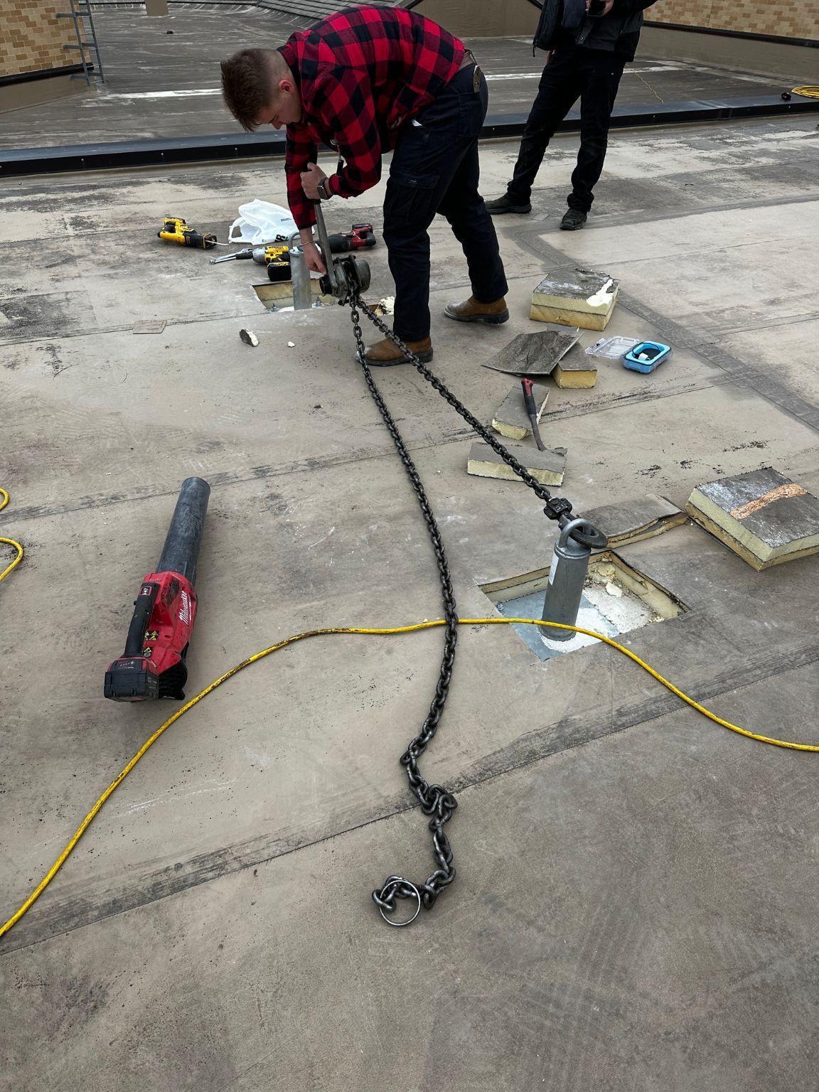 A man in a plaid shirt is working on a chain on the ground.