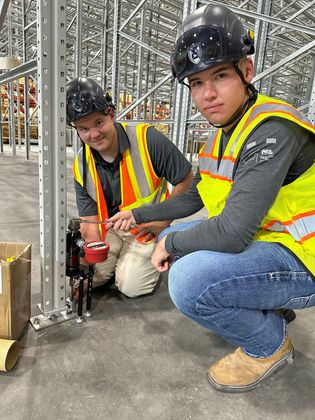 Two men in safety vests are working in a warehouse.