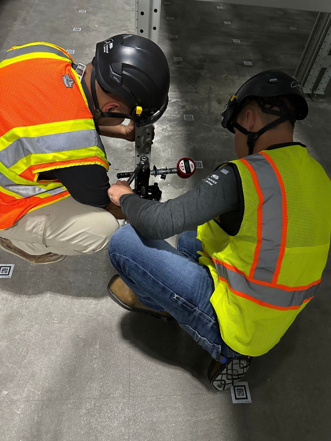 Two men wearing safety vests and helmets are working on a machine.
