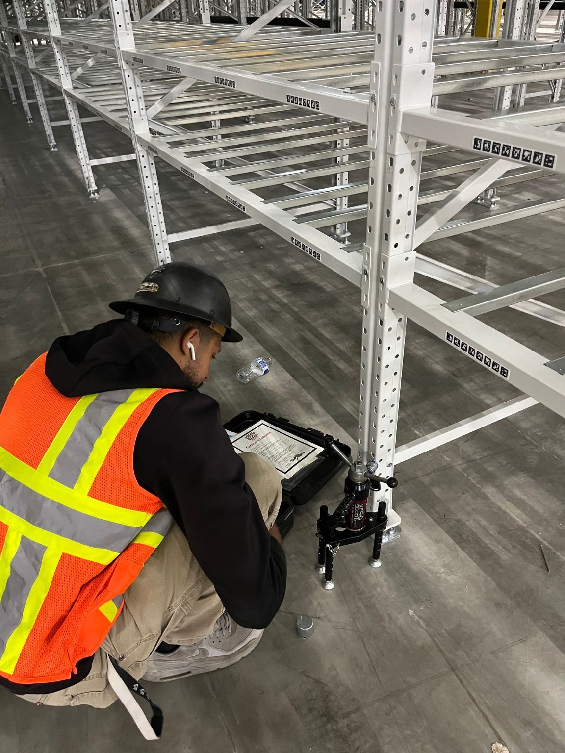 A man is kneeling down in a warehouse looking at a tablet.