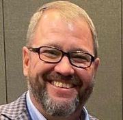 A man with a beard and glasses is smiling for the camera.