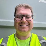 A man wearing glasses and a yellow vest is smiling for the camera.