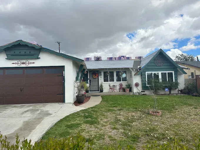 House with brown garage door and green trim, partly covered by a cloudy sky. Lawn with walkway.