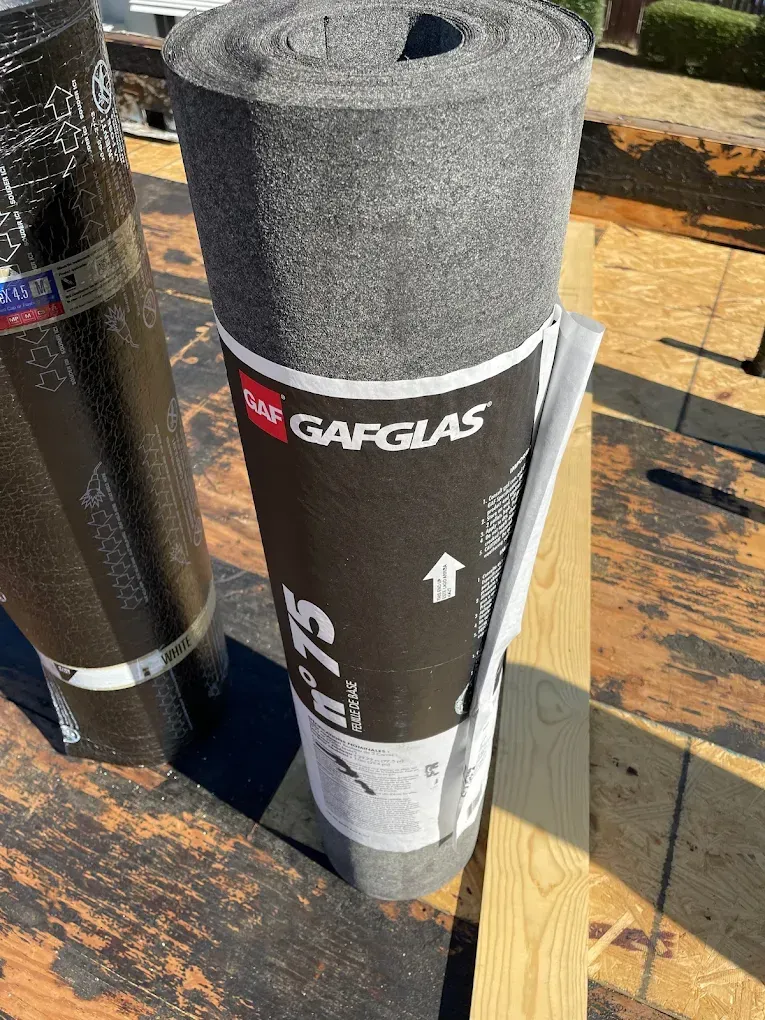 Roll of GAFGlas roofing material on a wooden surface, with other rolled materials in the background.