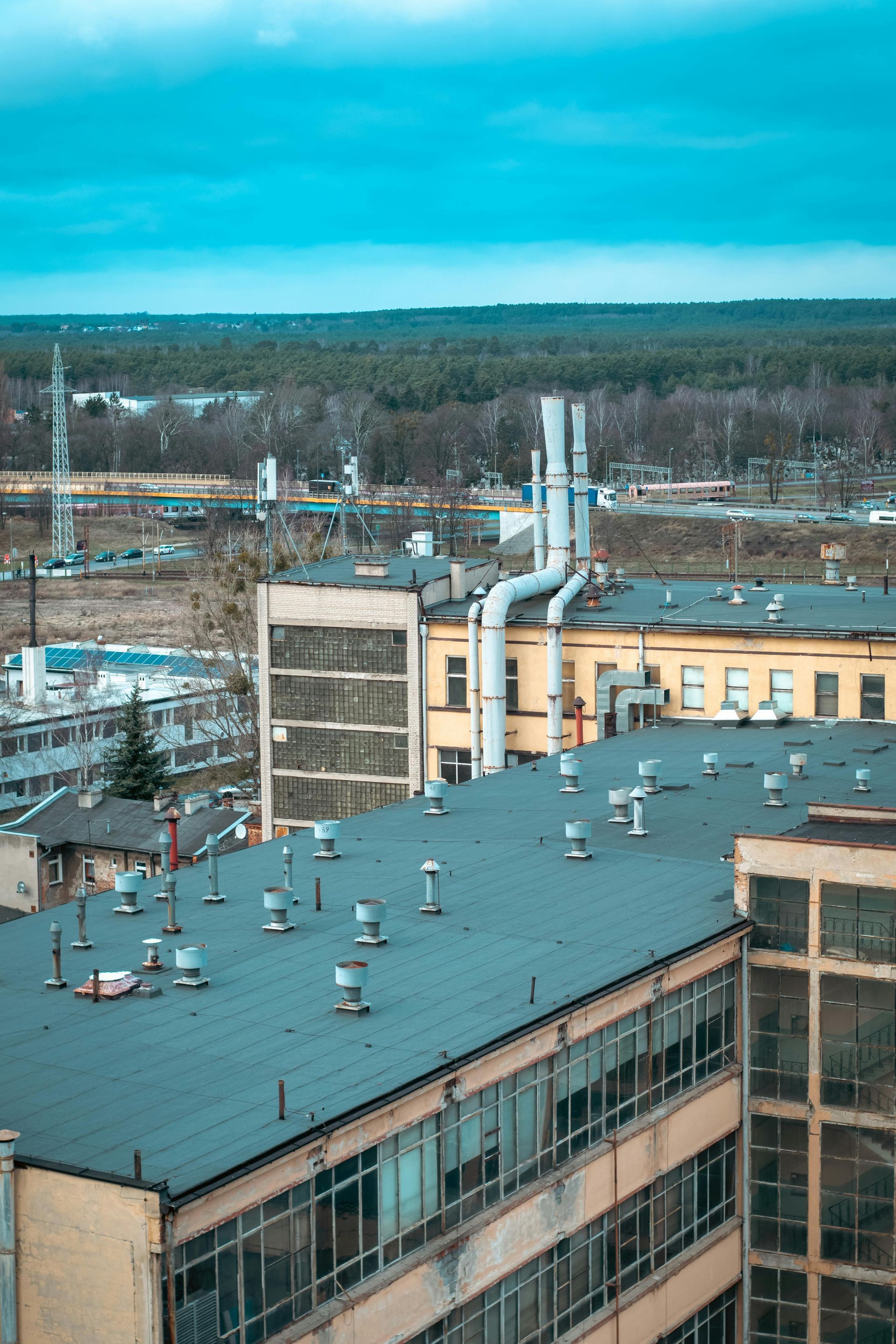 Overhead shot of industrial buildings with smokestacks, a blue sky, and a distant forest.