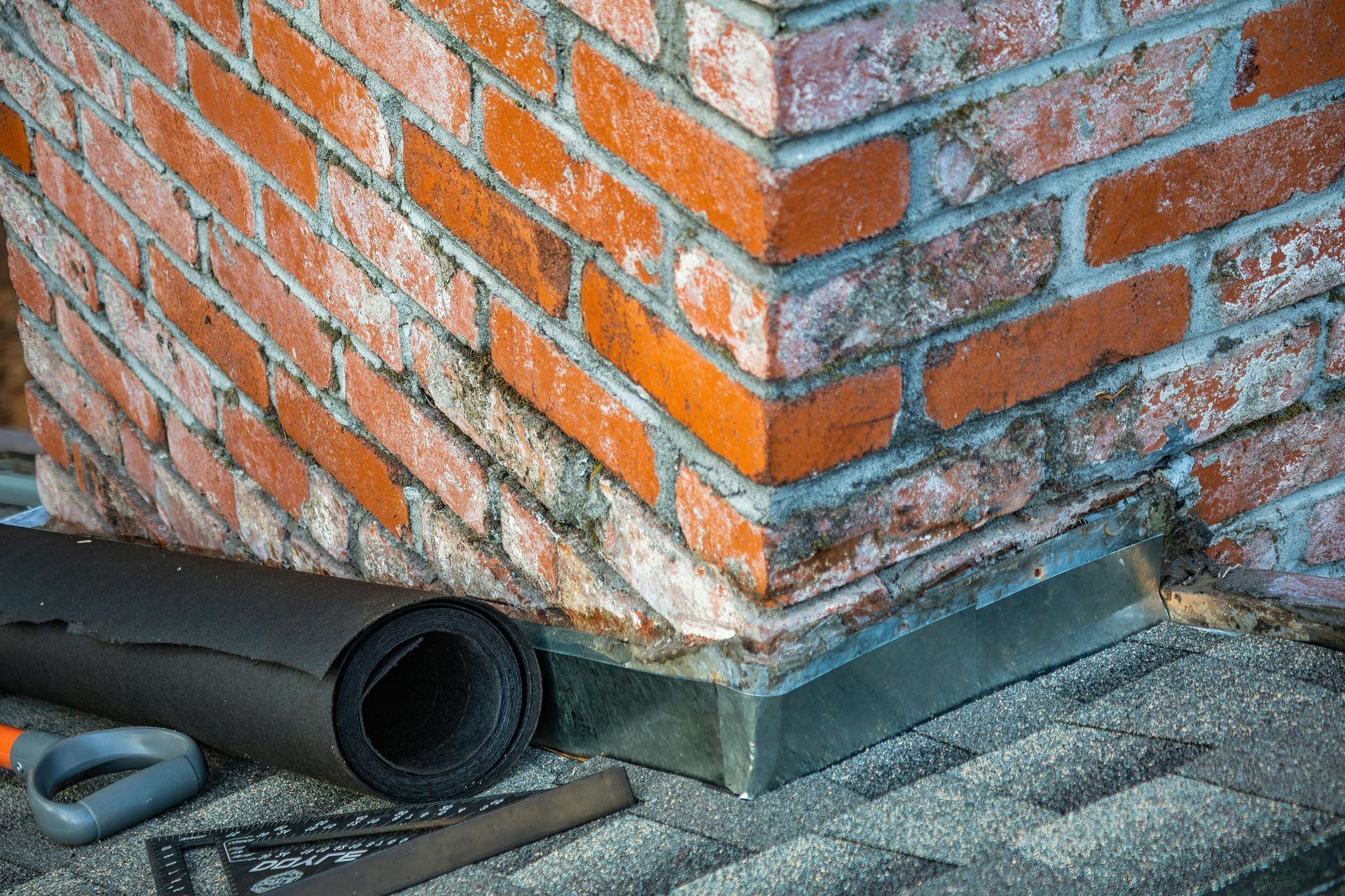 A brick wall with a roll of rubber and tools on the ground.