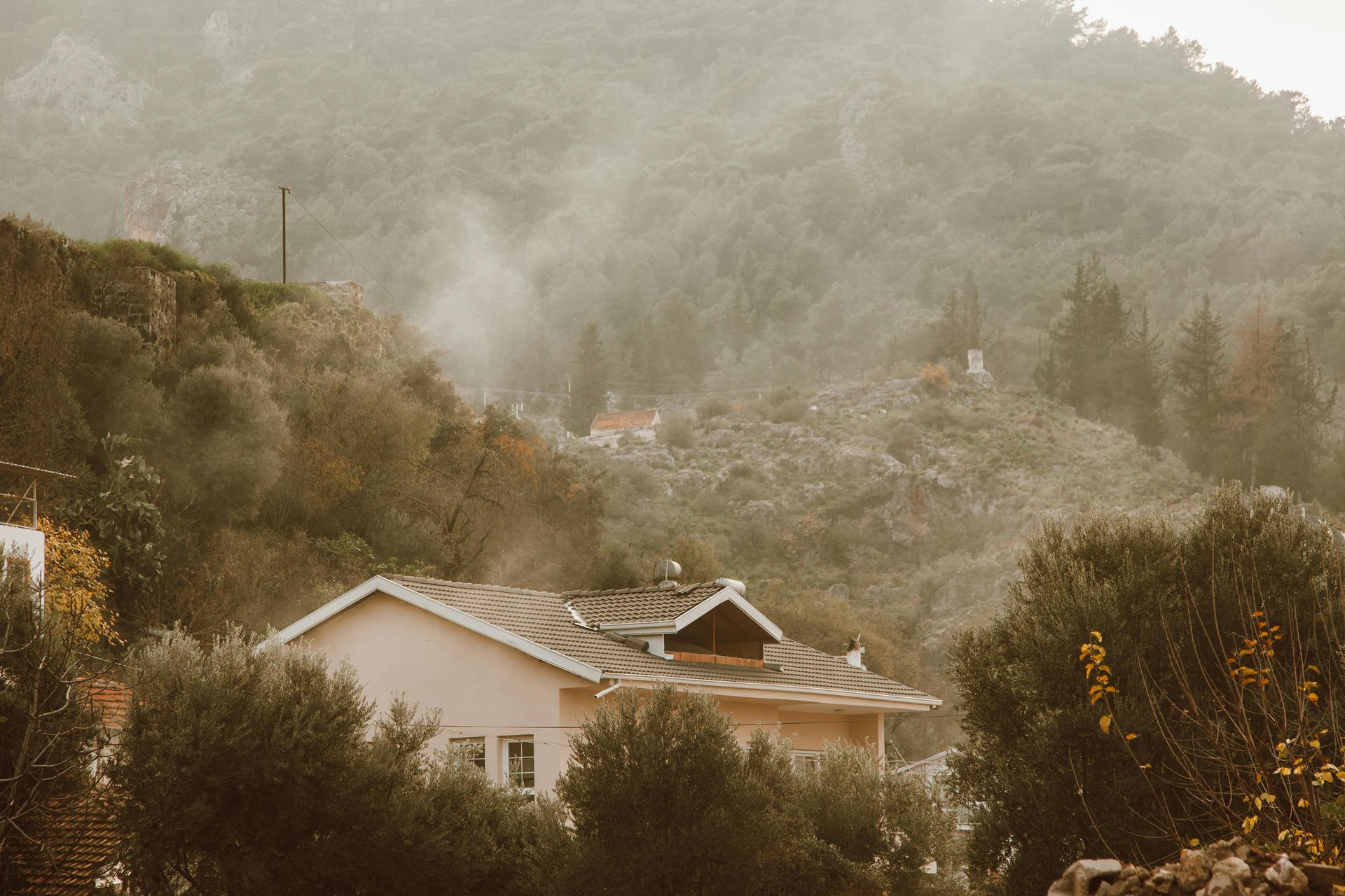 House with a smoking roof, amidst trees and a hazy mountain backdrop in Chino Hills, CA.