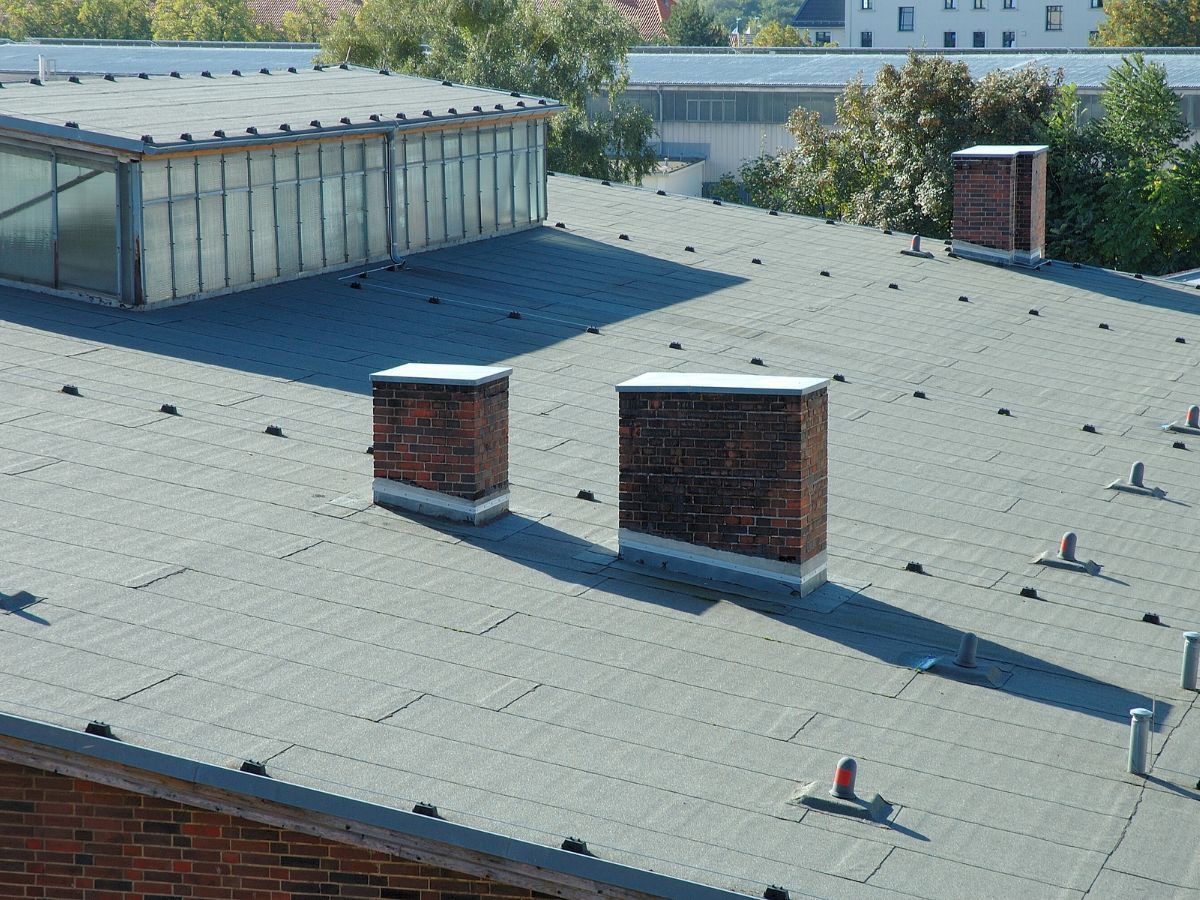 Gray rooftop with two brick chimneys and a skylight, in an urban setting.