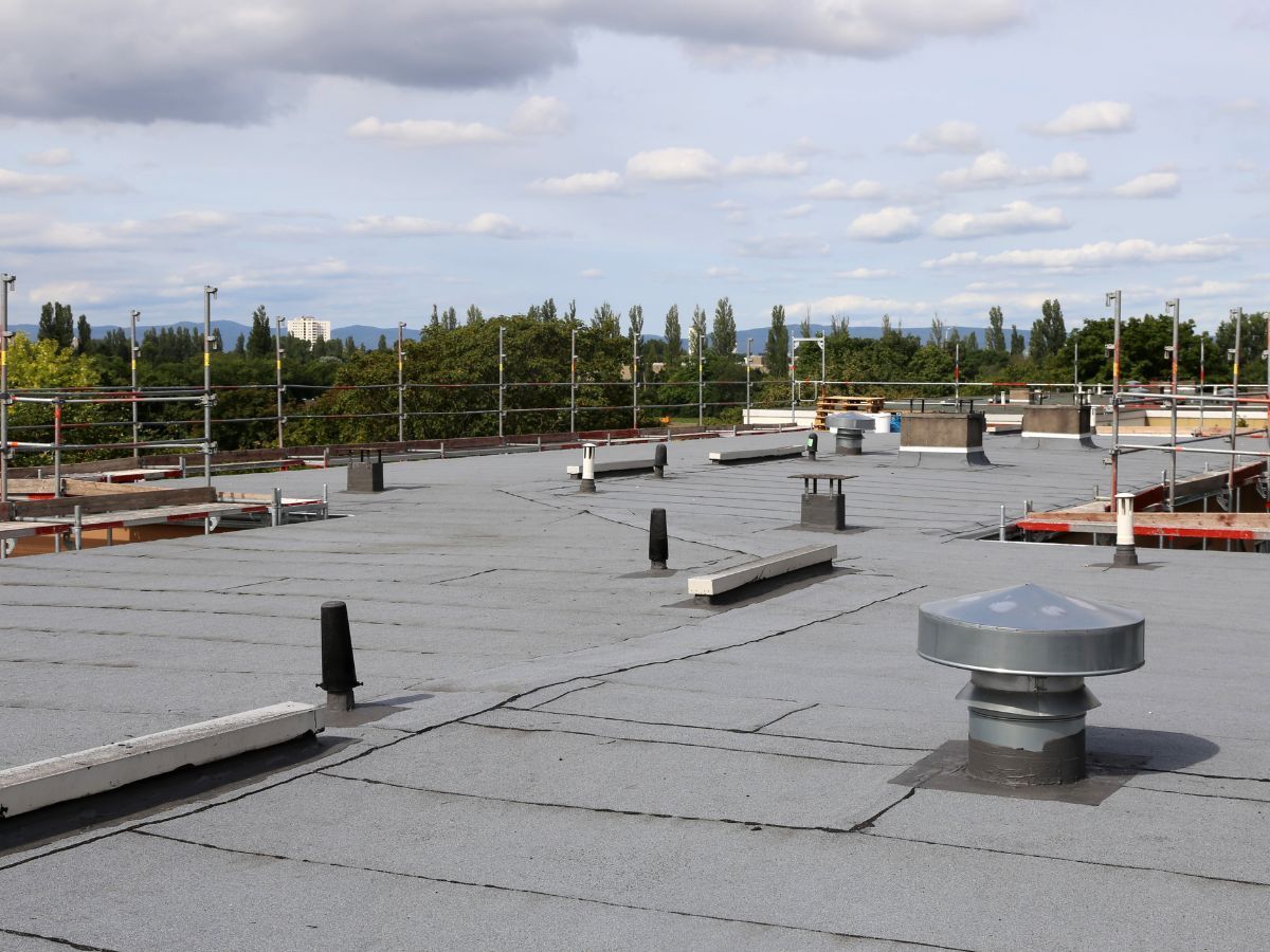 Flat rooftop with safety rails and vents against a cloudy sky.