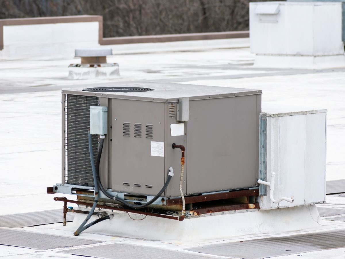 Rooftop HVAC unit, gray and white, on a white TPO roof, with vents and other equipment.