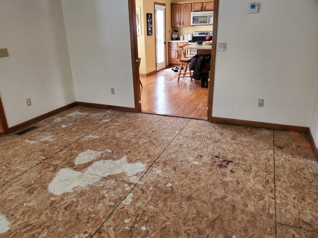 A room with a wooden floor and a kitchen in the background.