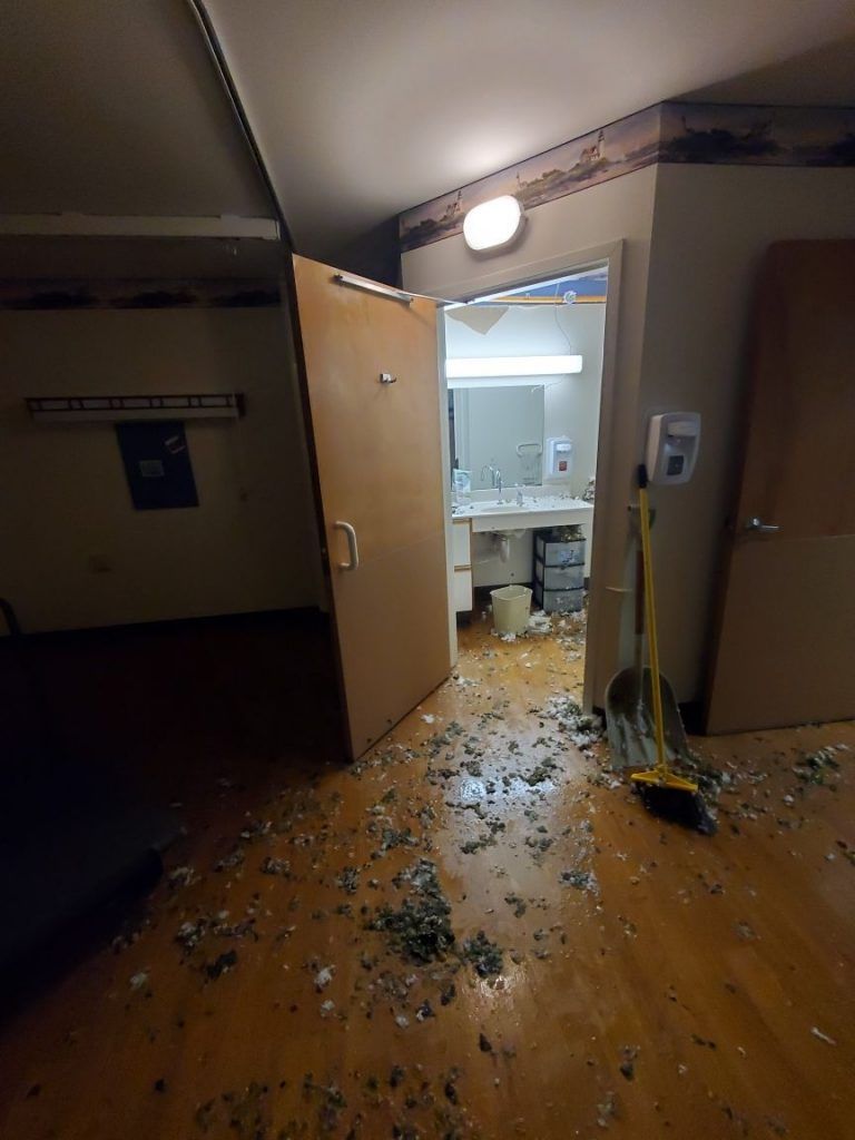 A water damaged room with broken glass on the floor and a broom.