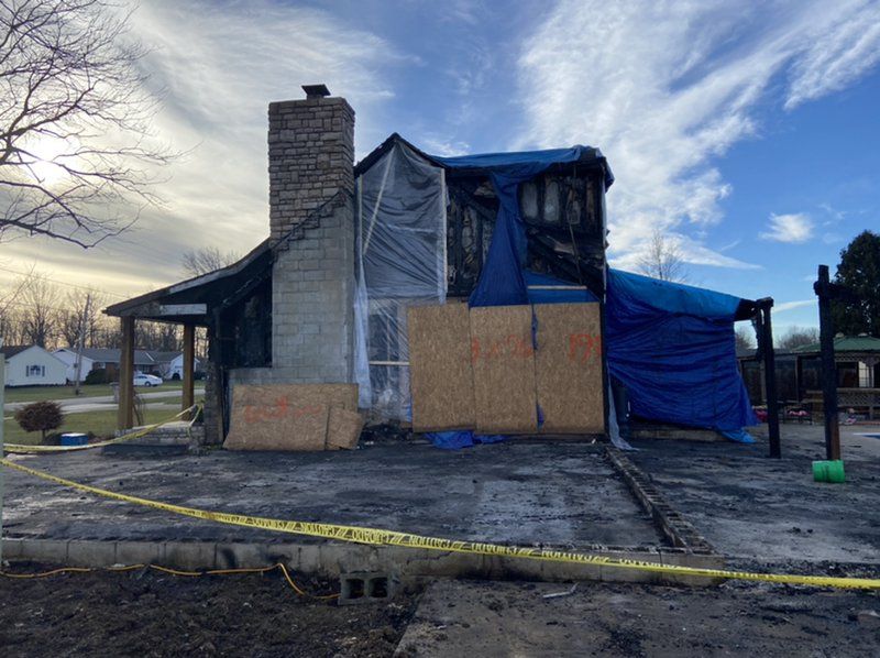 A house that has been damaged by a fire is covered in blue tarps.