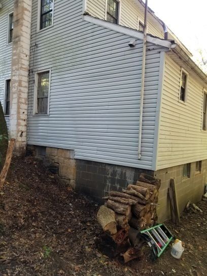 A pile of logs are sitting in front of a house.