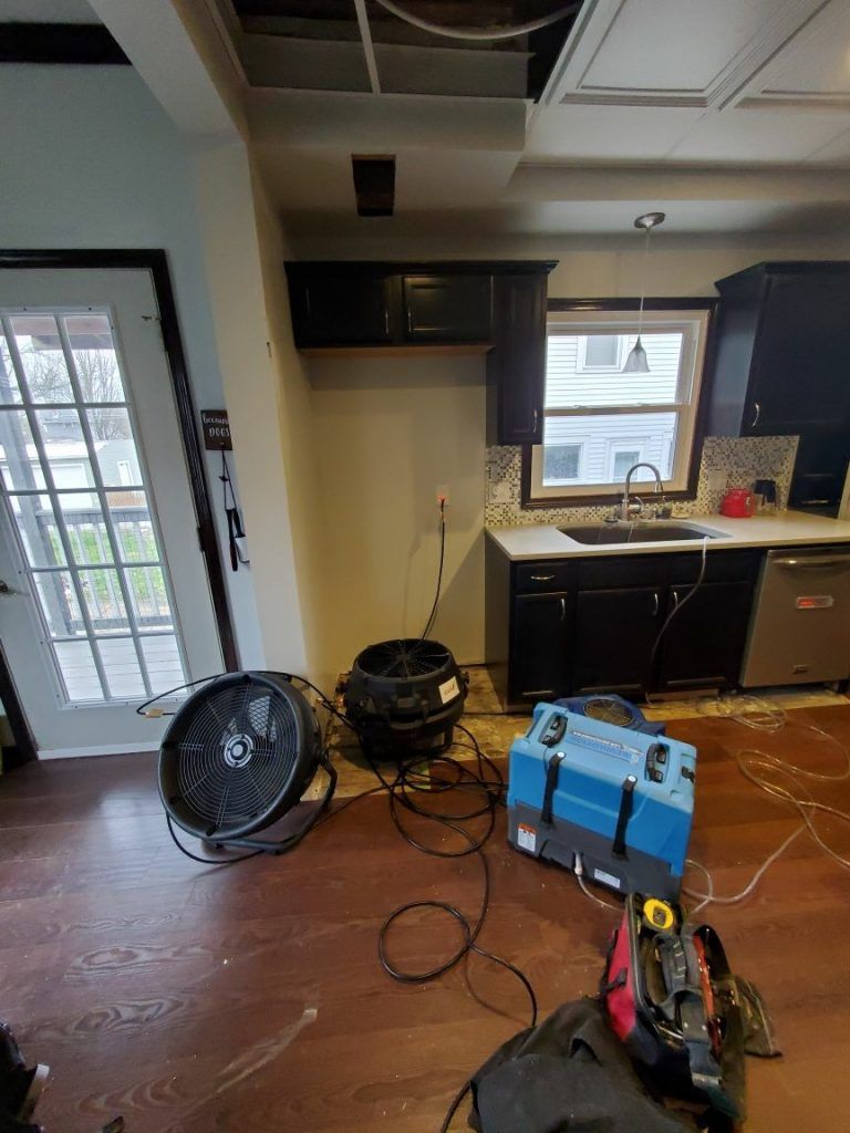 A kitchen with a fan and a blue toolbox on the floor.