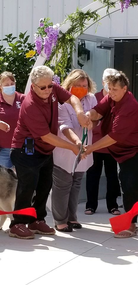 A group of people are holding large scissors together and cutting a red ribbon.