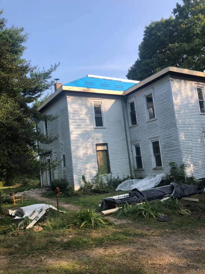 A large white house with a blue tarp on the roof.