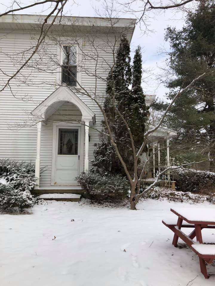 A white house with a picnic table in front of it in the snow.