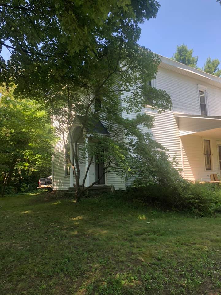 A white house with a porch and trees in front of it.