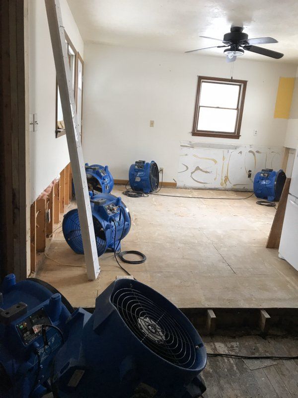 A water damaged room with windows and industrial blue fans.