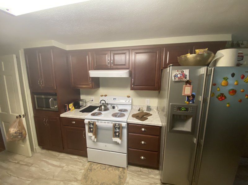 A kitchen with a stove ,wood cabinets, refrigerator , and microwave.