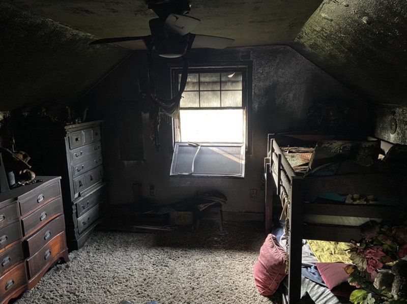 A fire damaged bedroom with two bunk beds , a dresser , and a window.