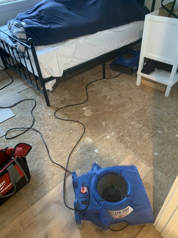 A blue industrial vacuum is sitting on the floor in a bedroom next to a bed.