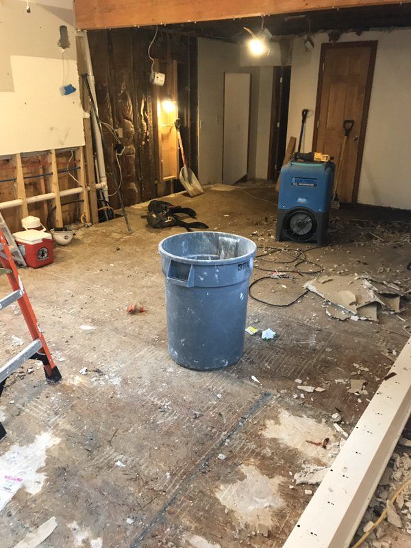 A blue trash can is sitting in the middle of a water damaged room.