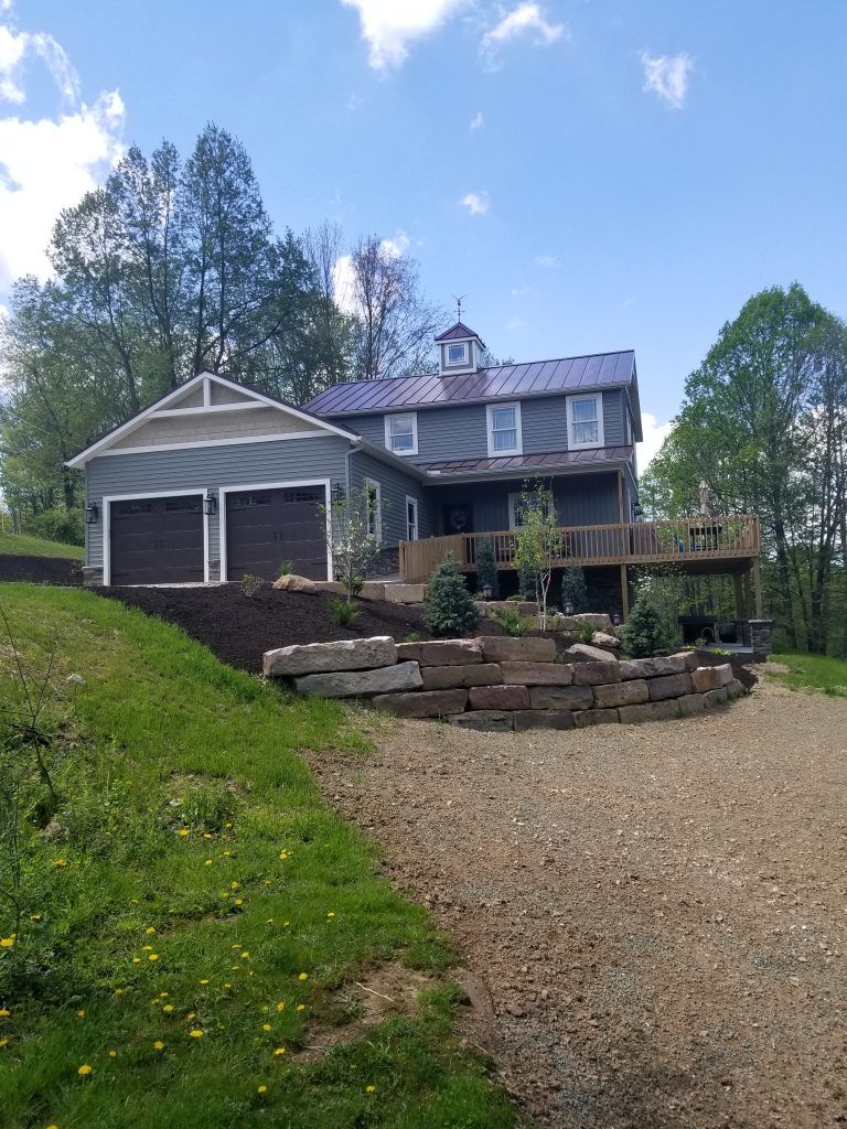 A large house is sitting on top of a hill next to a gravel driveway.