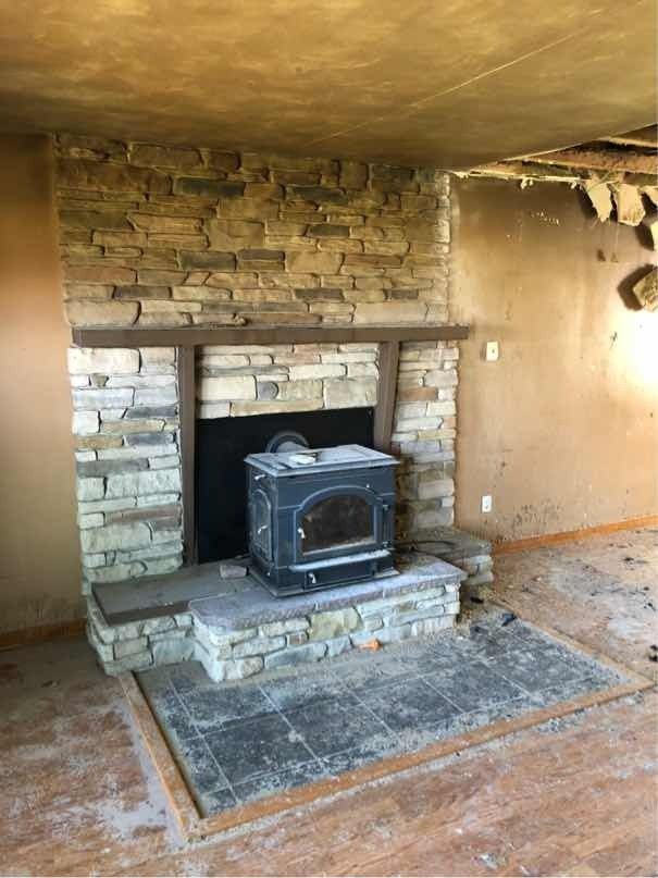 A stone fireplace with a wood stove in a living room.