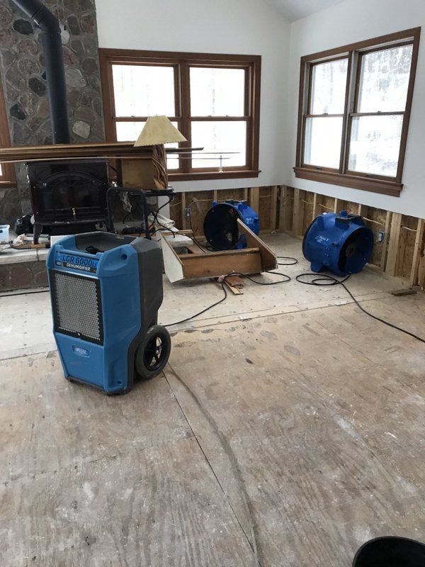 A water damaged room with windows and industrial blue fans.