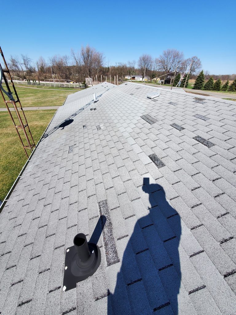 A shadow of a person is cast on the roof of a house with shingles.