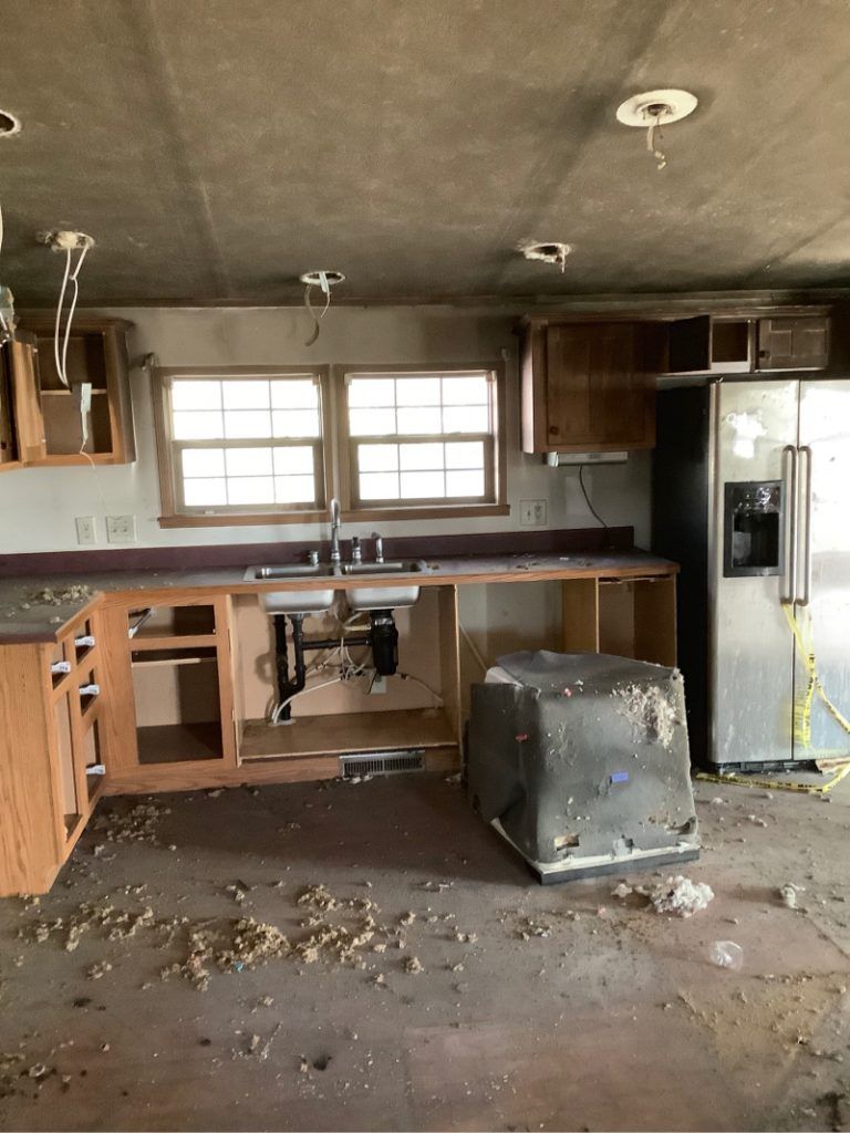 An empty kitchen with a stainless steel refrigerator and wooden cabinets after a fire.