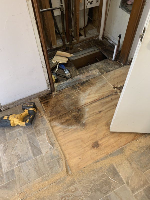 A drill is sitting on the floor next to a hole in the floor.