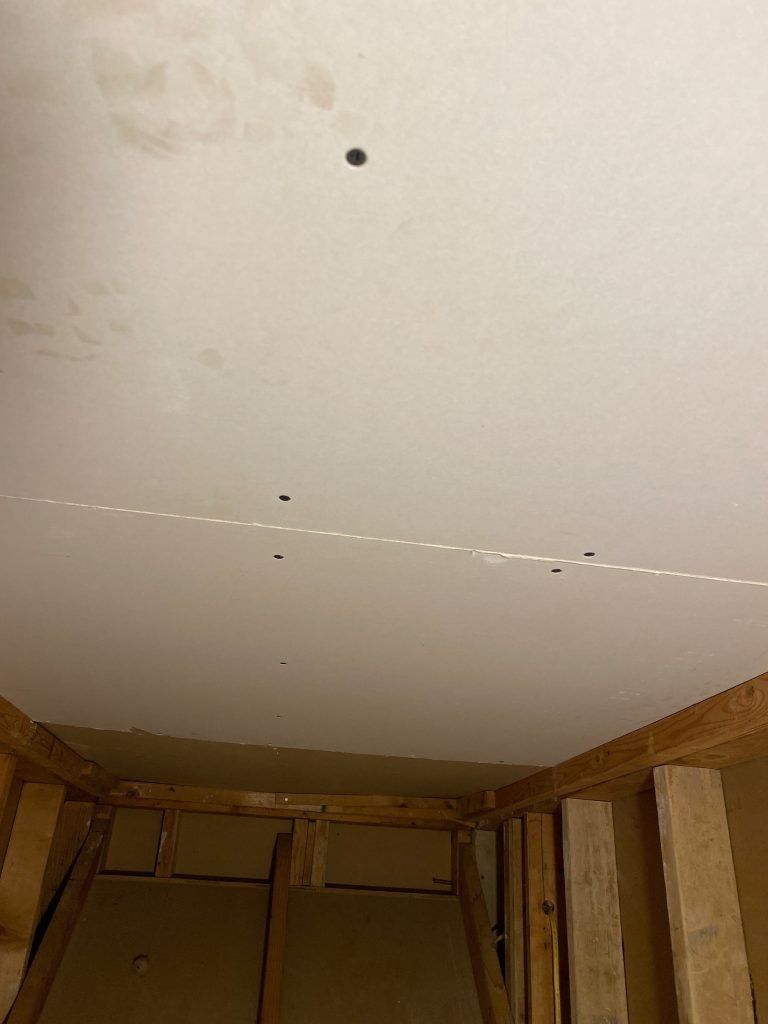A ceiling with a hole in it in a room and wooden beams.
